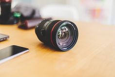 a camera lens sitting on top of a wooden table next to a cell phone and other electronics