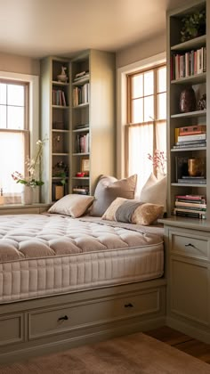 a bed sitting in the middle of a bedroom next to two windows with bookshelves