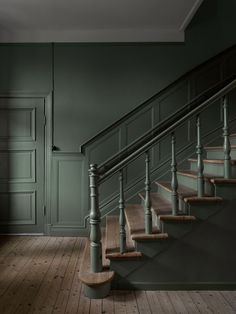 an empty room with green walls and wooden stairs in the center, along with dark wood flooring