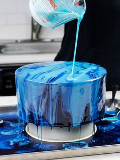 a person pouring blue liquid onto a cake