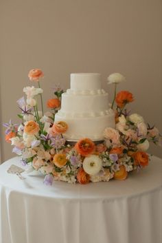 a three tiered wedding cake with flowers on the top and bottom is sitting on a white tablecloth