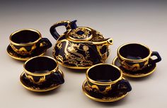 a black and gold tea set with four cups on the bottom one has a dragon design on it