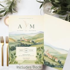 the wedding stationery is laid out on top of an envelope, with goldware and greenery