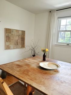 a wooden table with a plate on it in front of a window next to a chair