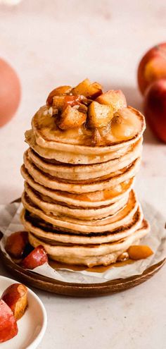 a stack of pancakes with apples and nuts on the top, next to two bowls of fruit