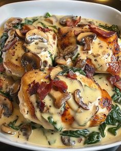 a white bowl filled with chicken covered in cheese and bacon on top of spinach