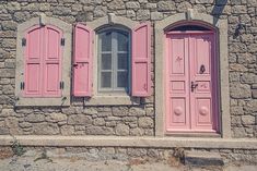 two pink doors and windows in front of a stone building with shutters on each side