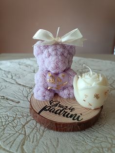 a purple teddy bear sitting on top of a wooden slice next to a white candle