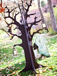 a metal tree with lanterns hanging from it's branches in the grass next to a grave