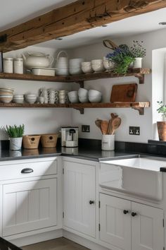 a kitchen filled with lots of white dishes and pots on top of wooden shelves next to a window