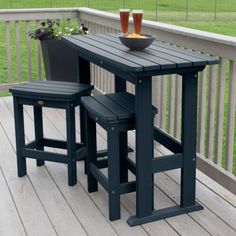 an outdoor table and two stools on a wooden deck with grass in the background