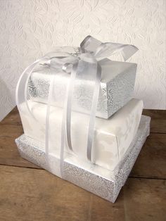 three white gift boxes stacked on top of each other with a ribbon tied around them