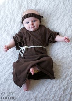 a baby laying on top of a white bed wearing a brown dress and headband