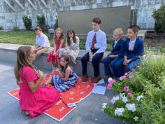 a group of young children sitting on top of a red blanket next to each other