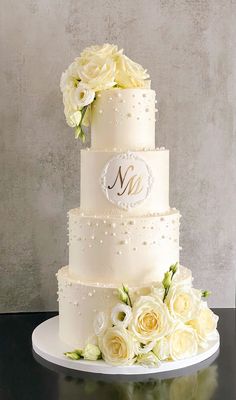 a three tiered wedding cake with white flowers and monogrammed initials on it