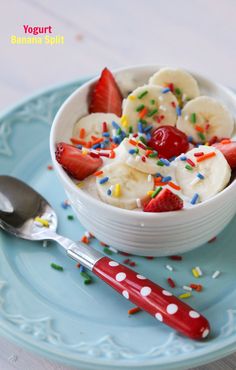 a bowl filled with bananas and strawberries on top of a blue plate next to a spoon