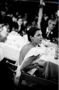 a black and white photo of a woman sitting at a table with people in the background