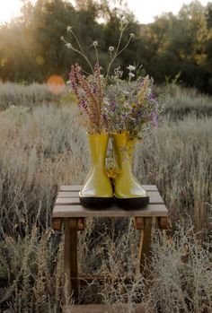 a pair of yellow rain boots sitting on top of a wooden table in a field