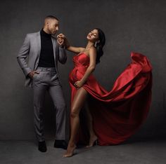 a man standing next to a woman in a red dress on a gray background with her legs spread out