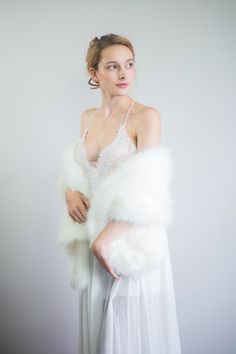 a woman is wearing a white dress and holding a fur shawl over her shoulder