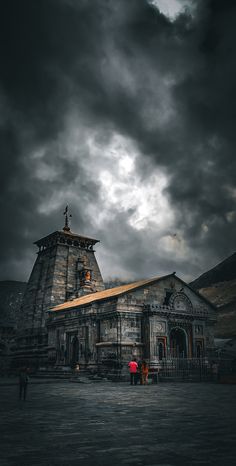 two people standing in front of an old building under a cloudy sky with dark clouds