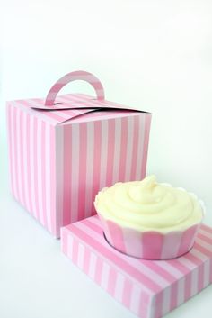 a pink and white striped box with a cupcake in it next to the box