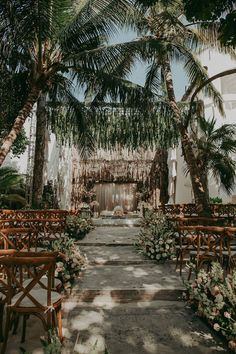 an outdoor wedding setup with wooden chairs and greenery on the aisle, surrounded by palm trees