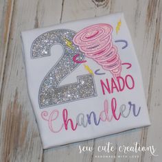 a birthday shirt with the number two on it and sparkles in the air, next to a wooden background