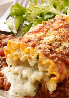 a white plate topped with lasagna covered in sauce and cheese next to a salad