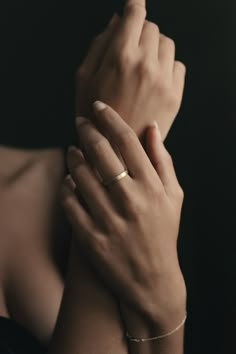 a woman's hands with two gold rings on her wrist and one holding the other hand