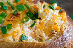 a baked potato with cheese and green onions on it's side, sitting in a bread bowl