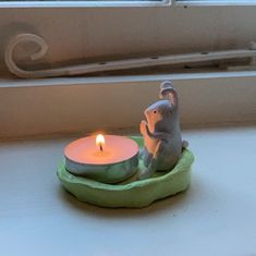 a small elephant figurine sitting on top of a green plate next to a lit candle