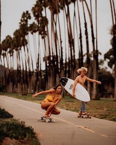 two women in swimsuits riding skateboards down a street with palm trees behind them