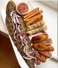 a plate with fish, potatoes and french fries on it next to some ketchup