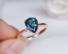 a woman's hand holding an engagement ring with a blue heart shaped stone