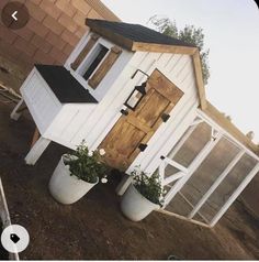 a small white house sitting on top of a dirt field next to a brick wall