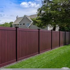 a brown vinyl fence in front of a house with green grass and trees on the side