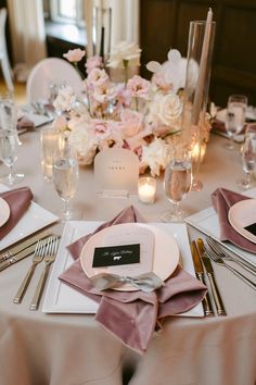 the table is set with white and pink flowers, silverware, and napkins