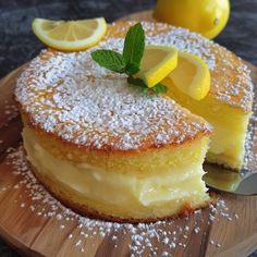 a lemon cake with powdered sugar and fresh mint leaves on top, sitting on a wooden plate