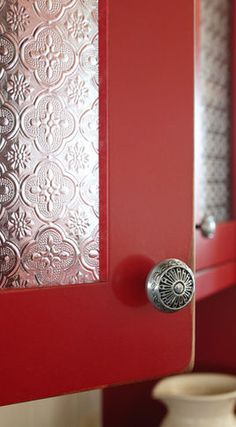 a close up of a red cabinet door with a vase in the corner behind it