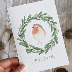 a hand holding up a christmas card with a bird in a wreath on the front