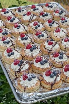 a tray filled with pastries covered in berries and whipped cream on top of each other