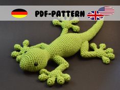 a green crocheted gecko laying on top of a black surface with the german flag in the background