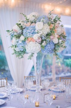 a tall vase filled with blue and white flowers on top of a dining room table