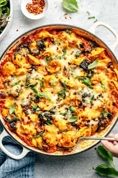 a large pan filled with pasta and spinach on top of a white table next to other dishes