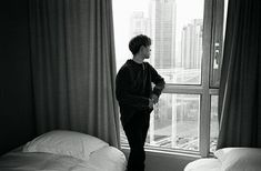 a man standing in front of a window looking out at the city outside his bedroom