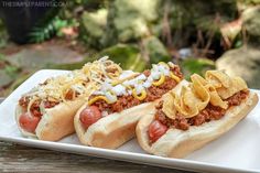 three chili dogs with cheese and onions on a white plate