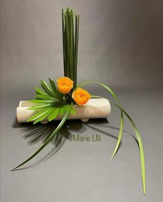 two yellow roses are sitting on top of a white vase with green grass and orange flowers