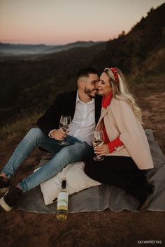 a man and woman sitting on top of a blanket holding wine glasses