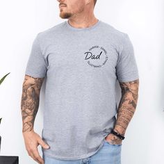 a man standing in front of a white wall wearing a grey shirt with the word dad printed on it